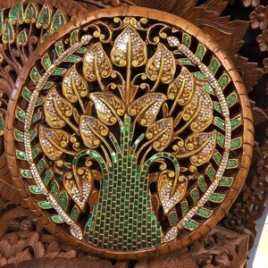 May include: A round wooden wall decor with a carved design of a tree with green and gold leaves. The tree is decorated with small, shiny, green and silver beads.