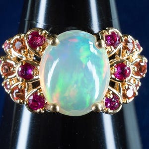 Op de afbeelding: Een gouden ring met een grote ovale opaal-edelsteen omringd door kleinere rode robijnen.
