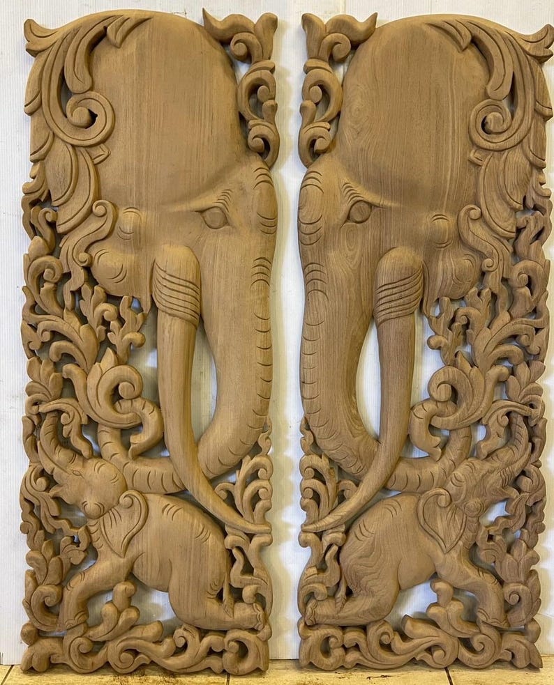 May include: A pair of intricately carved wooden wall panels featuring elephant heads with floral designs. The panels are made of light brown wood and have a traditional Thai style.