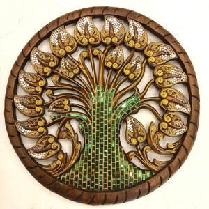 May include: A round wooden wall decor featuring a carved tree of life design. The tree is intricately detailed with gold and green mosaic tiles and has a circular frame.
