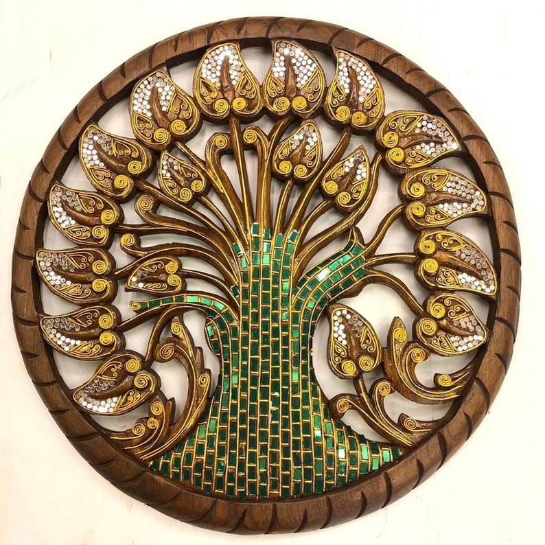 May include: A round wooden wall decor featuring a carved tree of life design. The tree is intricately detailed with gold and green mosaic tiles and has a circular frame.