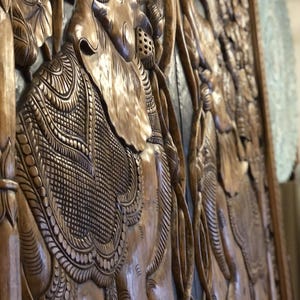 Puede incluir: Panel de madera tallada con elefantes y motivos florales. El relieve presenta patrones y texturas intrincados, mostrando la habilidad artesanal. La madera tiene un tono c&aacute;lido y natural, resaltando la profundidad y el detalle del dise&ntilde;o.