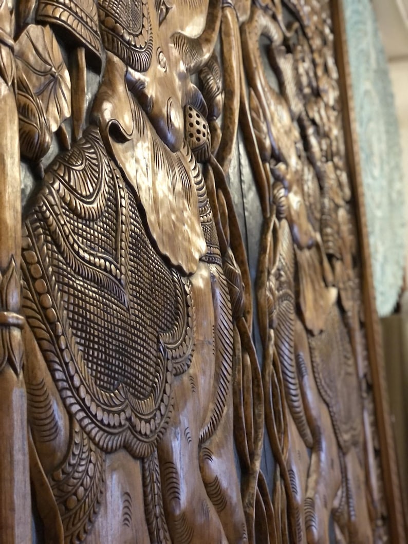 Puede incluir: Panel de madera tallada con elefantes y motivos florales. El relieve presenta patrones y texturas intrincados, mostrando la habilidad artesanal. La madera tiene un tono c&aacute;lido y natural, resaltando la profundidad y el detalle del dise&ntilde;o.