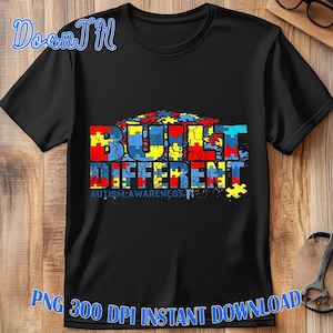 May include: Black t-shirt with the words "BUILT DIFFERENT" in colorful puzzle piece letters. The phrase "AUTISM AWARENESS" is below the main text. The shirt has a crew neck and short sleeves.