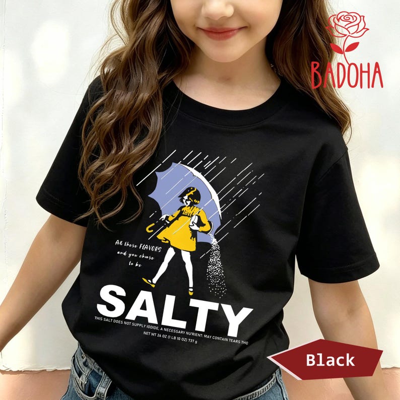 May include: Black t-shirt with a graphic of a girl under a blue umbrella, with the word "SALTY" in large white letters. The shirt also has text that reads "All these flavors and you chase to be".