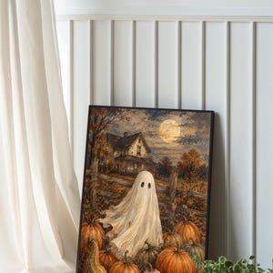 May include: A framed rectangular wall art print featuring a white ghost standing in a pumpkin patch at night. The scene includes a rustic wooden fence, a house in the background, and a full moon in the sky, all rendered in warm autumn tones.