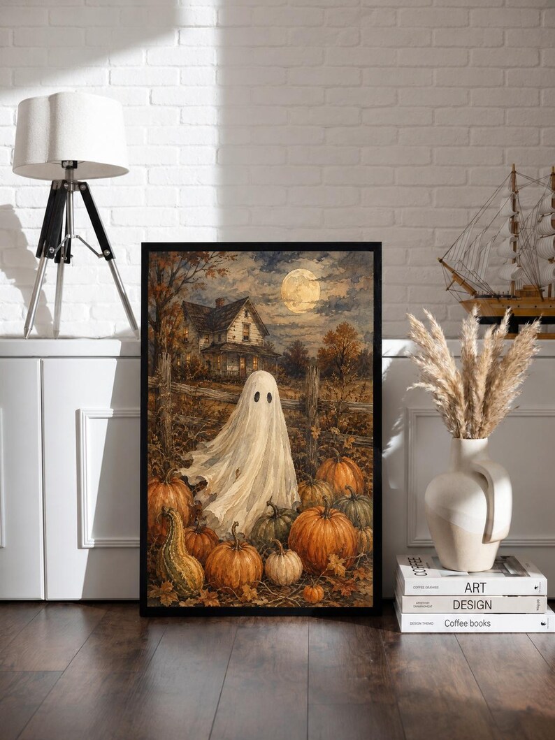 May include: A framed rectangular wall art print featuring a white ghost standing in a pumpkin patch at night. The scene includes a rustic house, a wooden fence, and a full moon in the background. The artwork uses warm orange, brown, and dark tones.