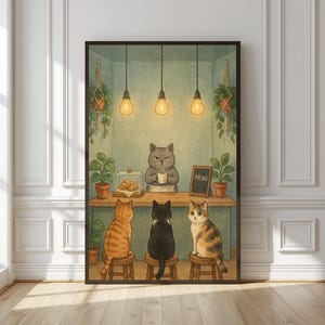 May include: A framed wall art print depicting a grey cat barista behind a counter holding a white mug. Three cats sit on stools facing the counter. The scene includes hanging pendant lights, potted plants, a pastry display, and a menu board.