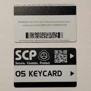 Könnte beinhalten: Zwei rechteckige Plastik-Keycards. Die obere Karte ist weiß mit einem schwarzen Streifen, dem Text SCPID<6.08<JAN<2023<b0K<111923b34b94<TbSCCC29<<<<<<, einer Warnung vor biometrischen Markern, einem Barcode und SCPID/UID(GES) JAN 2023 Property of The SCP Foundation. Die untere Karte ist schwarz-weiß mit SCP, Secure. Contain. Protect, einem QR-Code und 05 KEYCARD.
