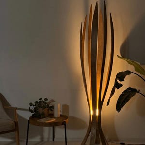 May include: A tall, wooden floor lamp with a unique design. The lamp features vertical, curved wooden slats that create an open, organic shape. The warm light shines through the slats, creating a cozy ambiance. The lamp is a decorative lighting fixture.