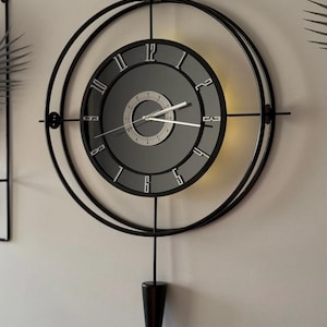 May include: A modern wall clock with a black metal frame and a gray face. The clock features a circular design with Roman numerals and a pendulum. The clock is approximately 20 inches in diameter.