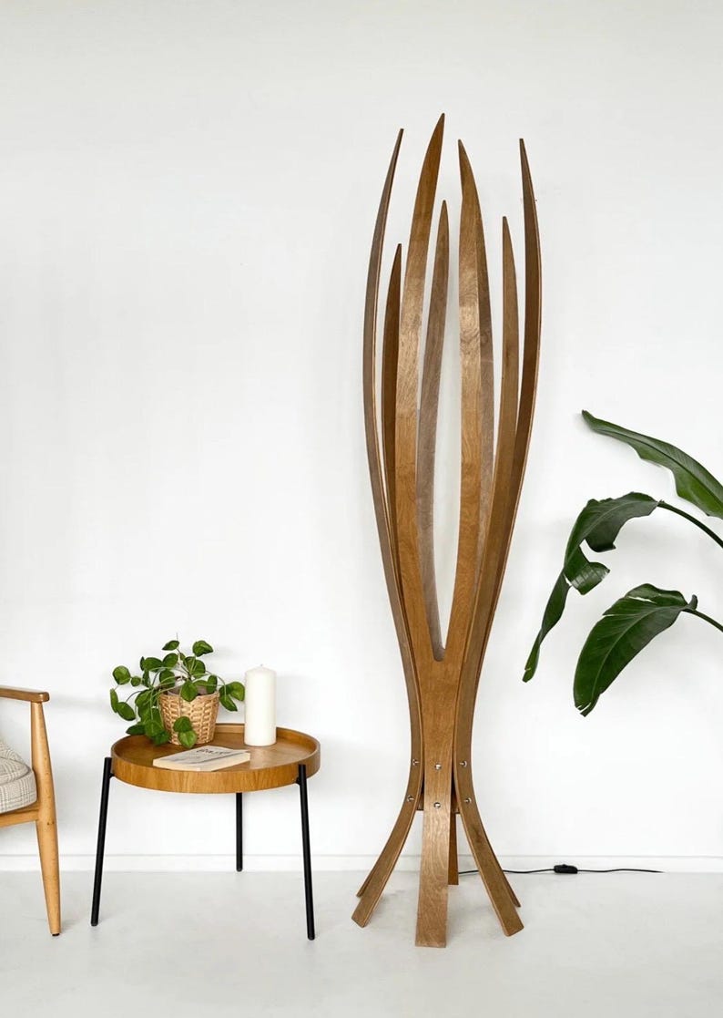 May include: A tall, wooden floor lamp with a unique, open design. The lamp features multiple vertical wooden slats that curve upwards, creating a sculptural, organic form. The lamp is made of light brown wood and stands on a base with multiple legs.