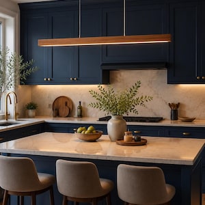May include: A modern kitchen with navy blue cabinets, a marble countertop island, and three beige bar stools. A wooden and gold rectangular light fixture hangs above the island. Decorative items include a vase with greenery and a wooden bowl with fruit.