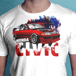 May include: White t-shirt with a red Honda Civic car graphic and the text "HONDA CIVIC" in bold, red letters. The car is shown with its hood open, set against a backdrop of a cityscape with blue and purple hues.