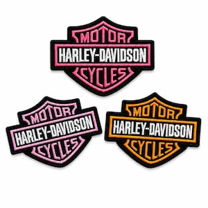 Può includere: Tre toppe ricamate con il logo Harley-Davidson Motor Cycles a forma di scudo. Una toppa presenta scritte e bordi rosa, una rosa chiaro e una arancione, tutte con testo bianco su sfondo nero.