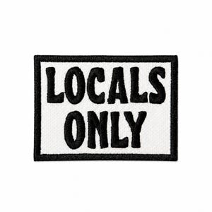 May include: A rectangular patch with the words "LOCALS ONLY" embroidered in bold, black letters on a white background. The patch has a black border and is likely designed to be sewn onto clothing or accessories.