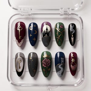 May include: A set of ten press-on nails with various designs, including a key, moon and stars, a castle, a rose, and a candle. The nails are in a clear plastic case. The color palette includes burgundy, navy, green, and black.