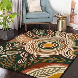 May include: A rectangular area rug with a nature-inspired design. The rug features a dark green background with brown, tan, and cream-colored leaf and circular patterns. The rug is placed on a dark wood floor.