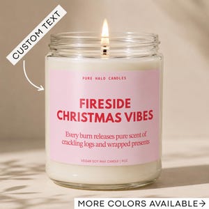 May include: A lit candle in a clear glass jar with a pink label. The label reads PURE HALO CANDLES, FIRESIDE CHRISTMAS VIBES, Every burn releases pure scent of crackling logs and wrapped presents, and VEGAN SOY WAX CANDLE | 9OZ. CUSTOM TEXT is visible.