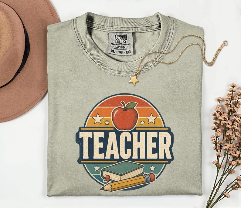 Folded Sandstone teacher shirt featuring a retro TEACHER graphic with apple, book, pencil, stars and vintage distressed school design.