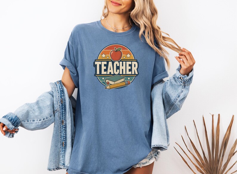 Woman wearing a Blue Jean teacher shirt with vintage TEACHER lettering, apple, book, pencil and distressed classroom graphic.