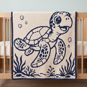 Puede incluir: Una manta de ganchillo color crema con un gráfico pixelado azul marino de una tortuga marina nadando entre plantas submarinas y burbujas. La manta tiene un borde azul marino sólido y está colocada sobre una cuna de madera clara.
