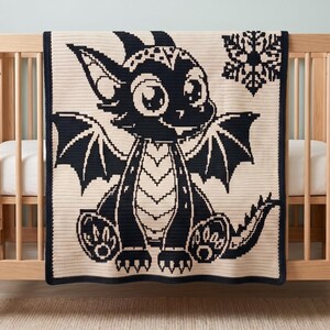 May include: A rectangular crochet blanket featuring a high-contrast black and cream design. The center displays a stylized cartoon dragon with large eyes and wings, accompanied by a single snowflake graphic in the upper right corner.