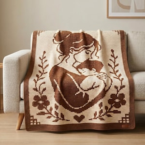 Könnte beinhalten: Gehäkelte Decke in Creme- und Brauntönen mit einem Mutter-Kind-Motiv. Die Decke ist mit einem floralen Muster und Herzen verziert und über einem Sofa drapiert. Sie strahlt Wärme und Geborgenheit aus.
