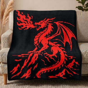 May include: A rectangular crochet blanket featuring a black background with a large, pixelated red dragon design. The dragon is depicted in profile, breathing fire from its mouth, with its wings spread and tail curled at the bottom of the blanket.