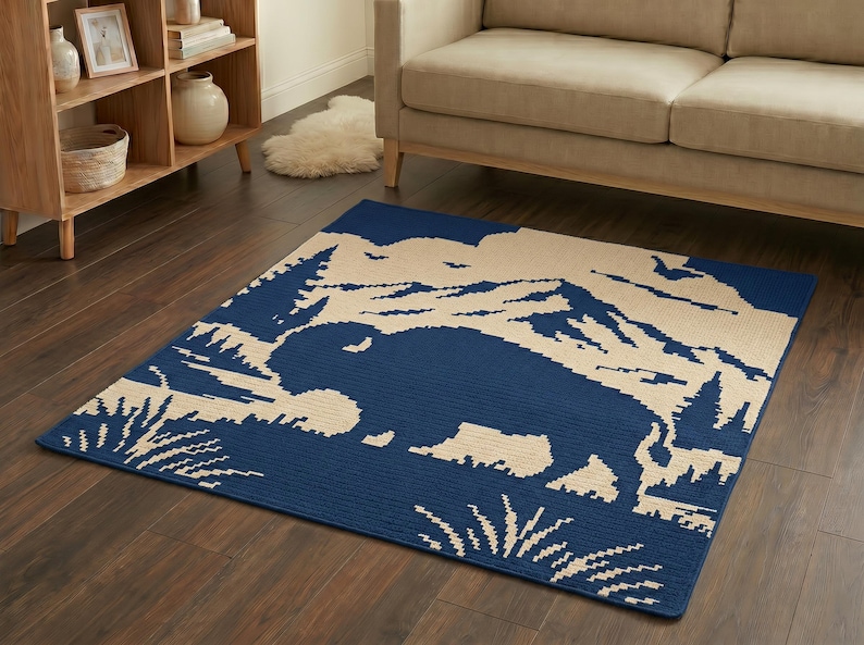Puede incluir: Una alfombra rectangular con un dise&ntilde;o azul y beige que presenta una silueta de bisonte, monta&ntilde;as y &aacute;rboles. La alfombra est&aacute; colocada sobre un suelo de madera oscura, con un sof&aacute; beige y una estanter&iacute;a de madera en el fondo.