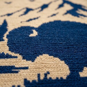Puede incluir: Primer plano de una alfombra texturizada con un dise&ntilde;o de monta&ntilde;a y bisonte. Las siluetas de bisonte y monta&ntilde;a son de color azul marino sobre un fondo beige. La alfombra tiene una textura suave y tejida.