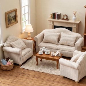May include: A miniature living room set featuring a beige and white striped sofa and two matching armchairs. A wooden coffee table holds a miniature tea set and an open book. A woven basket with yarn sits nearby on a wooden floor with a rug.