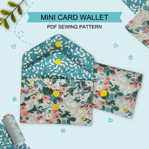 May include: A PDF sewing pattern for a mini card wallet featuring two fabric designs. One wallet is made from a light blue fabric with a colorful floral print and yellow snap buttons, while the other is a teal fabric with a white leaf pattern.
