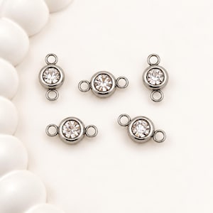 May include: Five circular jewelry connectors made of dark gunmetal-toned metal, each featuring a single clear, faceted round rhinestone set in the center. Each connector has two small circular loops on opposite sides for attachment purposes.