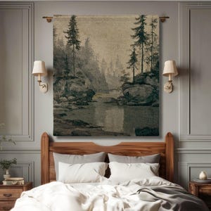 Puede incluir: Una estructura de cama de madera con un edredón blanco y una manta gris, colocada bajo un gran tapiz de pared que muestra un paisaje de pinos, acantilados rocosos y un río tranquilo en tonos tierra. El texto OAK ANTHOLOGY Fine Art Home Decor es visible.