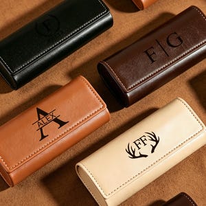 May include: A collection of rectangular, leather-like watch cases in black, dark brown, tan, and beige. Each case features a flap closure with white stitching and custom laser-engraved designs, including initials, names, and antler motifs.