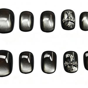 Könnte beinhalten: Ein Set aus zehn künstlichen Fingernägeln mit glänzendem, dunkelgrauem Katzenaugen-Effekt. Zwei der Nägel sind mit einem mittig platzierten, metallisch silberfarbenen Kreuz-Emblem verziert. Die Nägel sind in zwei Fünferreihen angeordnet.