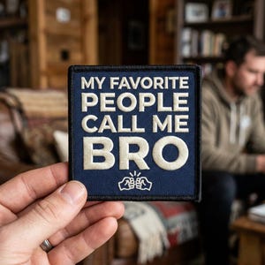 May include: A navy blue embroidered patch with white text that reads "MY FAVORITE PEOPLE CALL ME BRO." The patch has a black border and a small graphic of two fists bumping. The patch is held in a person's hand.