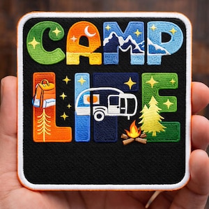May include: Embroidered patch with the words "CAMP LIFE" in colorful letters. The design includes a backpack, a camper, a campfire, a mountain range, and a pine tree. The patch has a black background and a white border.