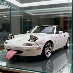 Può includere: Modello di auto cabriolet bianca con tetto nero e ruote cromate. L'auto ha fari a scomparsa e una lingua rosa. La parola "MIATA" è stampata sulla parte anteriore.