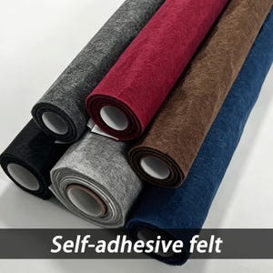 Pode incluir: Uma coleção de seis rolos de feltro autoadesivo em várias cores, incluindo preto, cinza escuro, cinza claro, vermelho profundo, marrom e azul marinho. Cada rolo apresenta uma superfície texturizada e é enrolado em um núcleo cilíndrico branco.