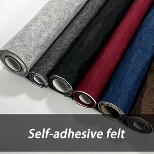 Puede incluir: Una colección de seis rollos de fieltro autoadhesivo dispuestos uno al lado del otro. Los colores incluyen gris claro, gris oscuro, negro, rojo intenso, azul marino y marrón. Cada rollo presenta una superficie texturizada y un núcleo central.