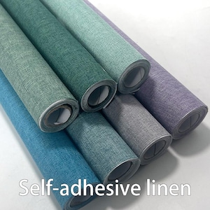 May include: A collection of rolled self-adhesive linen in various colors, including teal, green, gray, and purple. The rolls are arranged diagonally, showcasing the textured fabric. The text "Self-adhesive linen" is displayed at the bottom.