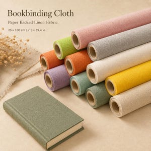 May include: A collection of paper-backed linen bookbinding cloth rolls in various colors including pink, gray, orange, green, yellow, and beige, alongside a single olive green book. The text reads Bookbinding Cloth, Paper Backed Linen Fabric, 20 x 100 cm / 7.9 x 39.4 in.