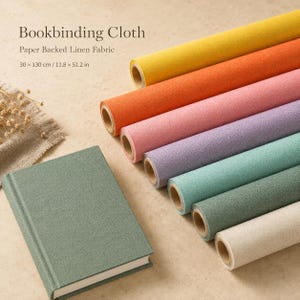 May include: A collection of paper-backed linen bookbinding cloth rolls in yellow, orange, pink, purple, teal, green, and beige, alongside a green-covered book. The text reads Bookbinding Cloth, Paper Backed Linen Fabric, 30 x 130 cm / 11.8 x 51.2 in.