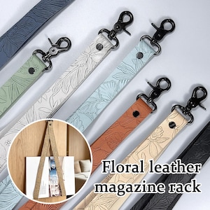 May include: A collection of floral embossed leather straps in various colors including sage green, white, light blue, tan, beige, and black, each featuring a black metal swivel lobster clasp and a black rivet for hanging magazines or books.
