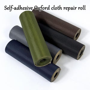 Pode incluir: Rolos de reparação de tecido Oxford autocolantes em várias cores. A imagem mostra rolos de tecido em tons de verde, azul marinho, cinza, preto e castanho. Os rolos estão bem enrolados e prontos para uso. O texto "Self-adhesive Oxford cloth repair roll" é visível.