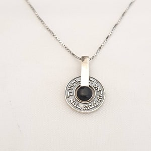 May include: A silver necklace with a pendant featuring a black onyx stone surrounded by Hebrew lettering.