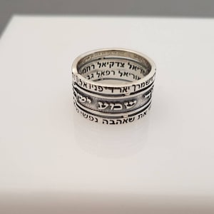 May include: A silver ring with Hebrew text inscribed around the band. The text is in a traditional Hebrew font and is arranged in four lines.
