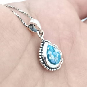 May include: A silver pendant necklace featuring a teardrop-shaped pendant with a light blue, speckled stone. The pendant is framed with a beaded border and hangs from a delicate chain. The necklace is shown against a neutral background.